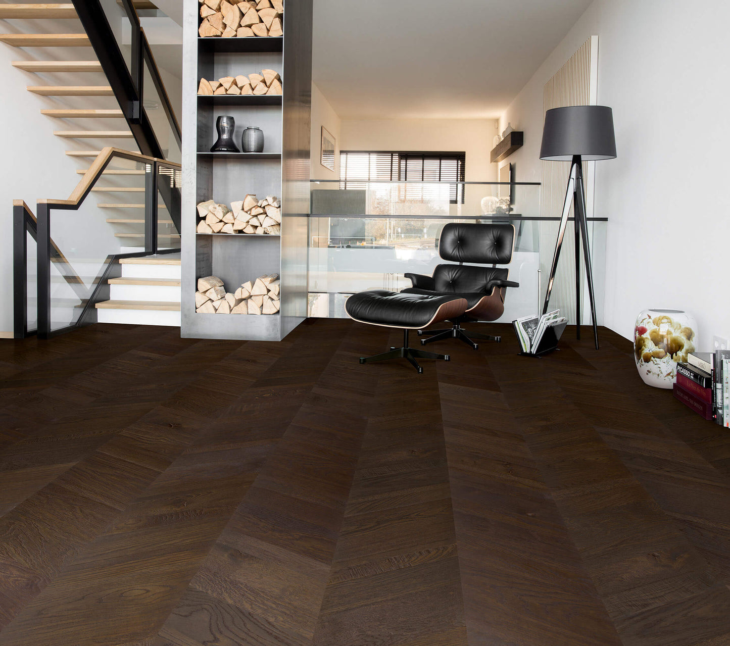 Modern interior with a black leather chair, wooden staircase, and bookshelf.