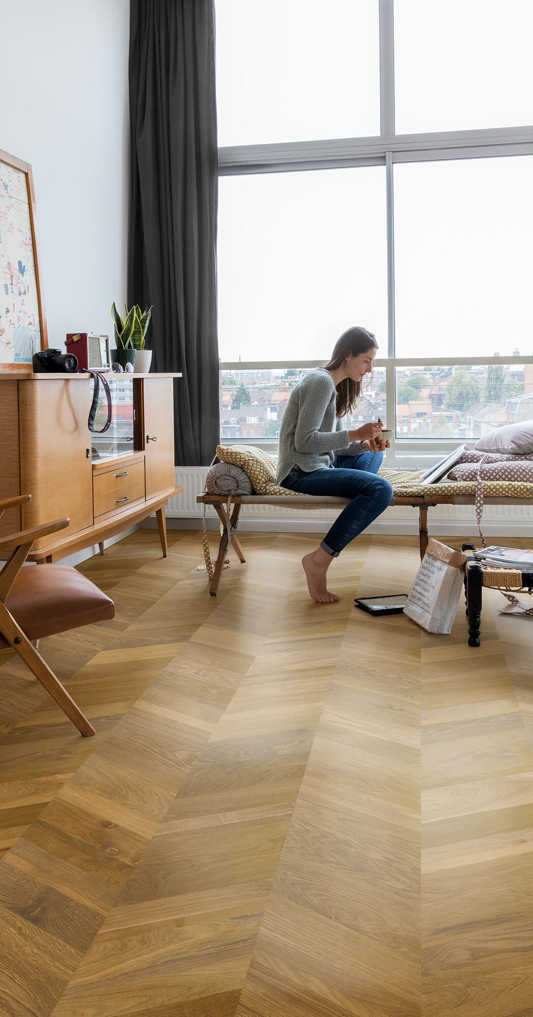 Woman sitting on a wooden floor in a modern living room with large windows.