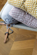 Close-up of a wooden stool with patterned cushions on a wooden floor.