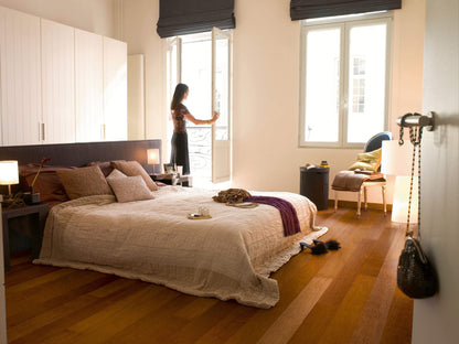Woman standing by a window in a bedroom with a bed and wooden floor.