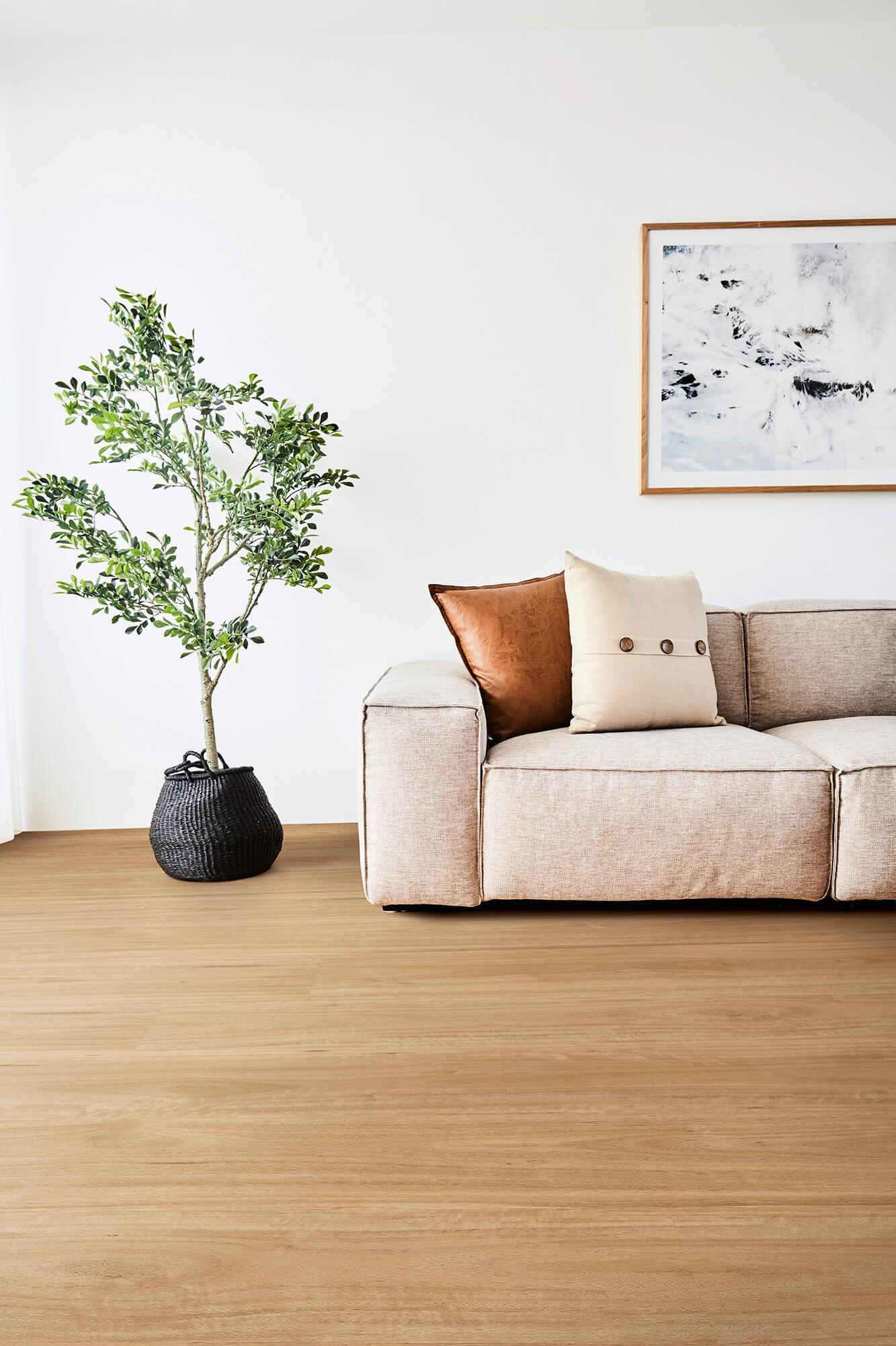 Modern living room with a beige sofa, decorative pillows, and a plant on a wooden floor.