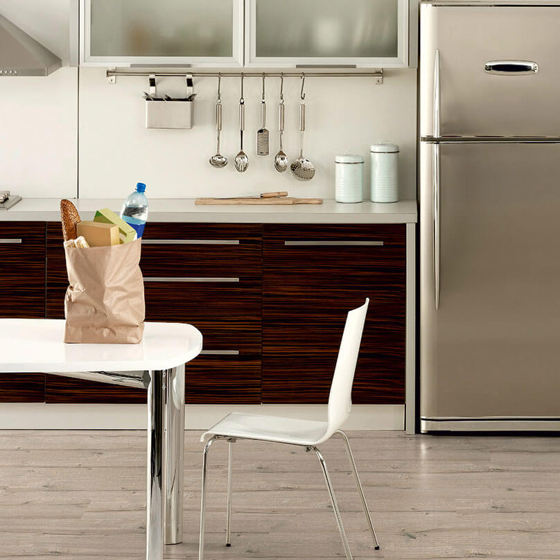 Modern kitchen with stainless steel refrigerator, wooden cabinets, and a small table with a bag.